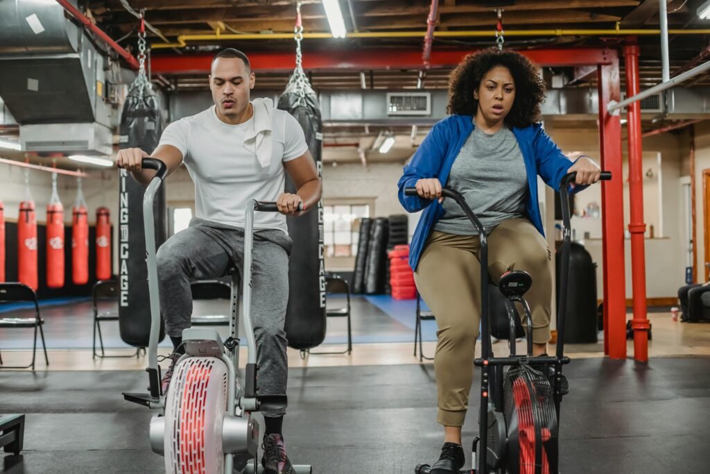 Man and woman doing a stationary cycling exercise in a gym, focusing on endurance and progress tracking helps for lose weight
